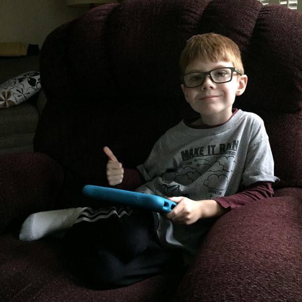Connor sitting in the recliner playing tablet in his new glasses